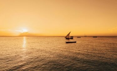 Serene sailboat scene with a golden sunset over the Indian Ocean in Zanzibar, Tanzania.