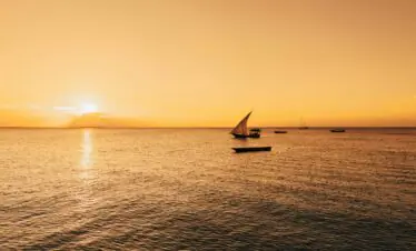 Serene sailboat scene with a golden sunset over the Indian Ocean in Zanzibar, Tanzania.