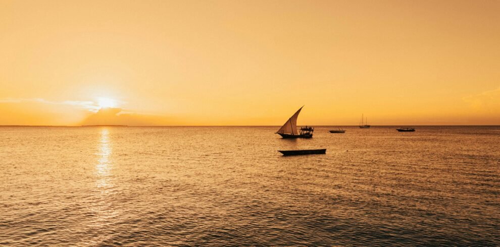 Serene sailboat scene with a golden sunset over the Indian Ocean in Zanzibar, Tanzania.