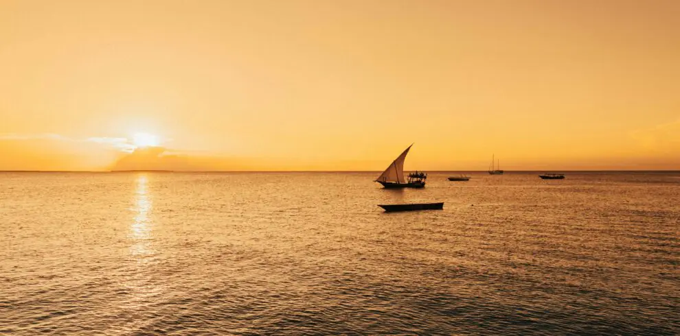Serene sailboat scene with a golden sunset over the Indian Ocean in Zanzibar, Tanzania.