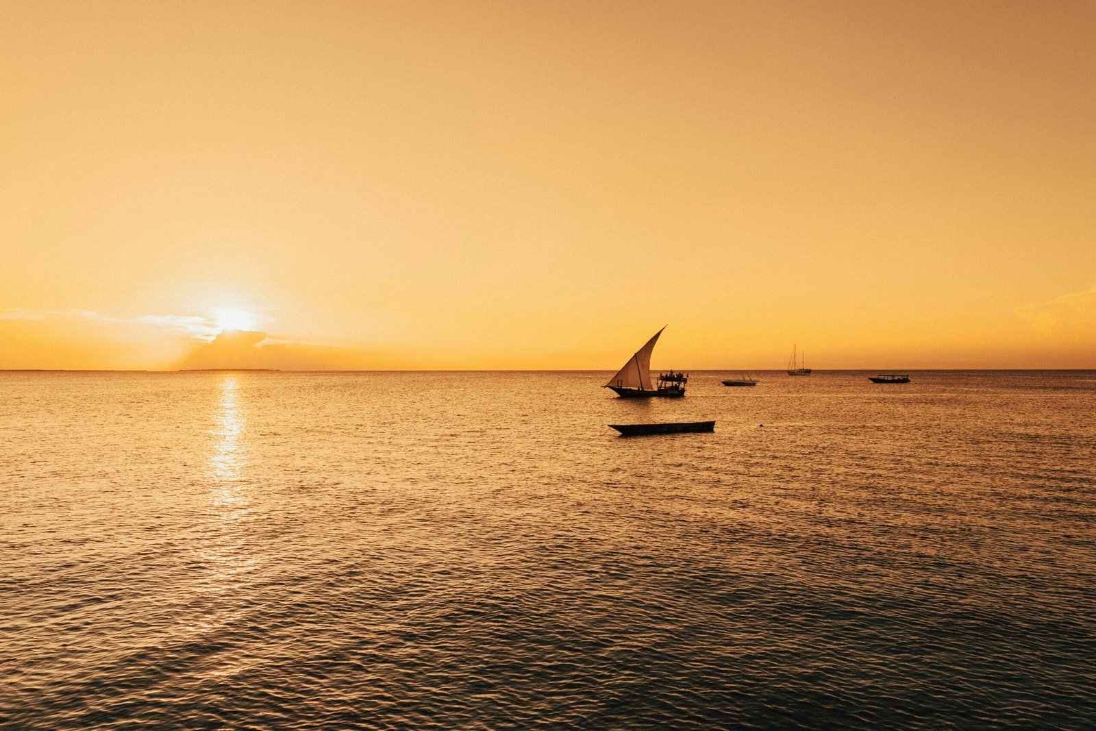 Serene sailboat scene with a golden sunset over the Indian Ocean in Zanzibar, Tanzania.