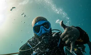 Scuba diver in Zanzibar's clear waters gives OK signal, surrounded by bubbles underwater.