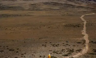 Lone hiker traversing the vast landscape of Mount Kilimanjaro under a clear sky.